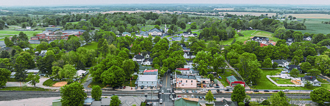 An aerial image of a rural town with a few homes, businesses, a school, and streets surrounded by agricultural land.