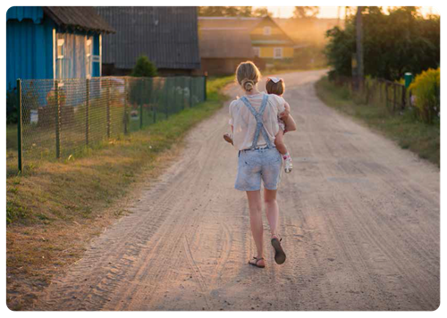 Mother carrying child on dirt road in countryside