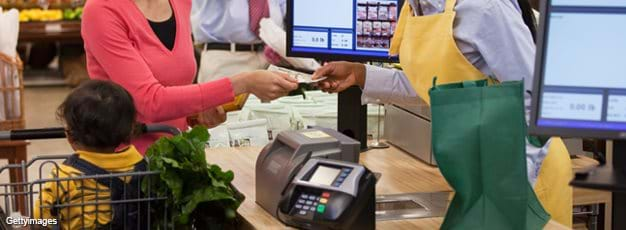 Mother with child in cart paying for groceries at checkout counter